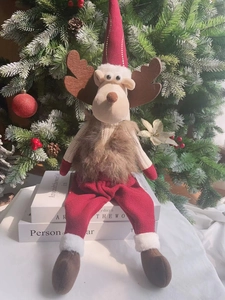 Nahaufnahme einer Weihnachtsrentier-Plüschpuppe, die auf Deko-Büchern am Baum sitzt