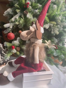 Detail einer sitzenden Weihnachts-Elchpuppe in rotem Hut auf Buch mit Feiertagsdekor