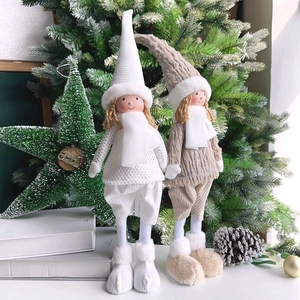 Close-up of plush Christmas angel dolls with knit hats and fur boots by a festive tree
