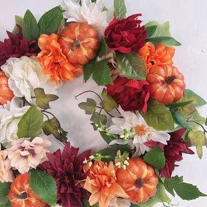 Close-up detail of realistic autumn wreath with mini pumpkins and dahlias on white wall