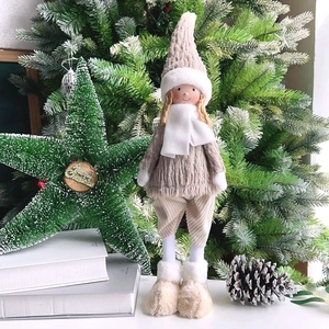 Detail of Christmas plush doll in beige sweater with white scarf near tree decorations