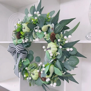 Detail of autumn wreath with eucalyptus leaves, pine cones, pumpkins, and a striped bow