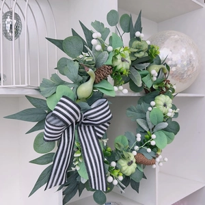 Detail of pumpkin wreath with eucalyptus leaves, pine cones and striped bow on white shelf