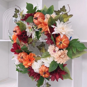 Detailed close-up of autumn wreath featuring orange pumpkins, maple leaves and dahlia flowers