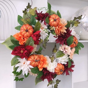 Close-up of autumn harvest wreath with orange pumpkins, dahlia flowers and green foliage