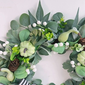 Autumn wreath with white pumpkins, green eucalyptus leaves and black white striped bow decoration