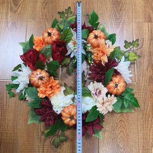 Detail of autumn wreath with orange pumpkins and red dahlias measuring 45cm on wood floor