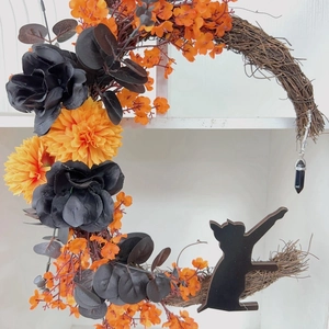 Close-up of crescent moon Halloween wreath with black cat silhouette and orange flowers