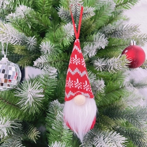 Detail of Christmas gnome ornament with knitted red hat hanging on snowy pine tree branch