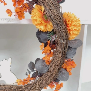 Detailed close-up of autumn harvest wreath with orange silk flowers and dried vines