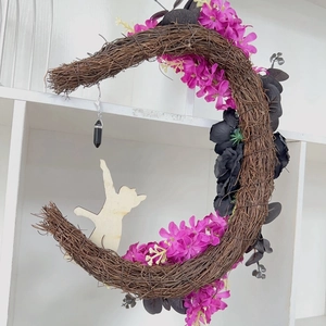 Detail of moon-shaped rattan Halloween wreath with purple flowers and a wooden cat silhouette