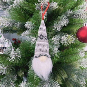 Detail of a knitted Christmas gnome ornament hanging on a festive tree with red berries