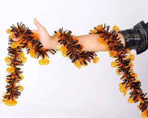 Detail of black and orange Halloween tinsel garland with pumpkin cutouts wrapped on arm