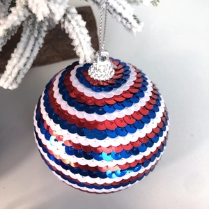 Vue rapprochée d'une boule de Noël à paillettes rouge blanc et bleu sur sapin enneigé