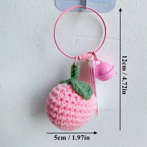 Detailed size view of a handmade pink peach crochet keychain with green leaves and bell