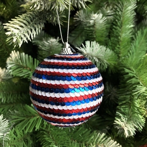 Gros plan d'une boule à paillettes rouge blanc bleu sur une branche d'arbre verte