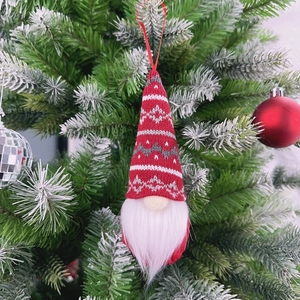 Charming red knitted Christmas gnome ornament with white beard hanging on a tree branch