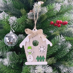 Close-up of wooden house-shaped Christmas ornament with snowman detail on green tree