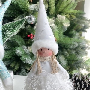 Detail of a white Christmas angel doll with sequins and faux fur on a snowy background