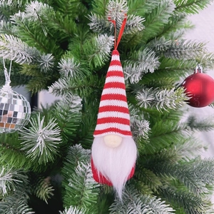 Hanging Christmas gnome ornament with red striped hat and white beard on a pine tree