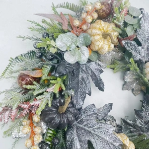 Close-up of glittery black maple leaves and white pumpkins on a festive wreath