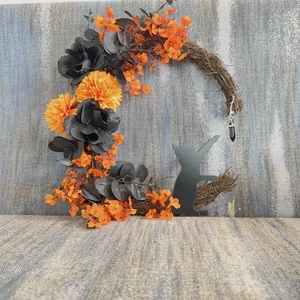 Macro detail of Halloween crescent moon wreath with orange flowers and black cat silhouette