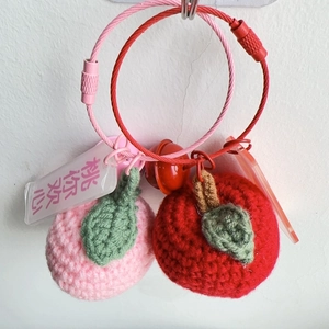 Detail of handmade crochet peach and apple keychains with metal rings and bells
