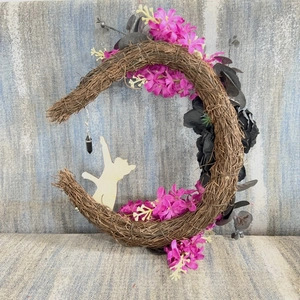 Detail showing natural brown rattan moon wreath with wooden cat silhouette and purple silk flowers