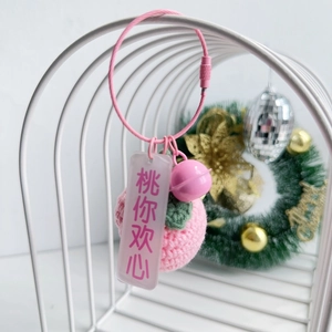 Detail of handmade knitted pink peach keychain with green leaf and small pink bell