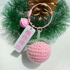 Detailed close-up of handmade crochet peach keychain with bell and acrylic charm