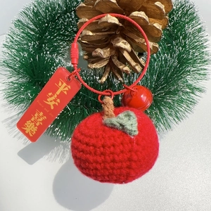Detail of red handmade crochet apple keychain with small bell and festive tag