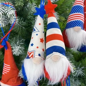 Close-up of patriotic gnome plush ornaments with star patterns hanging on pine branches