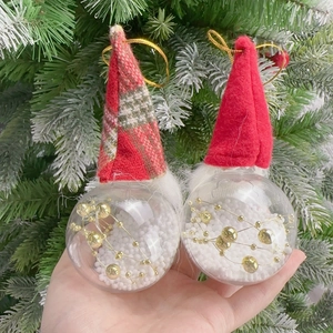 Close-up of two transparent Christmas baubles with Santa hats and snow filling decoration
