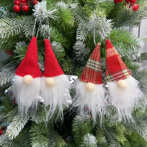 Detail of four Christmas gnomes with sequin accents and red hats hanging on a pine tree