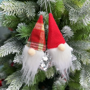 Detail of sequined gnome ornaments with faux fur beards hanging on a snowy Xmas tree