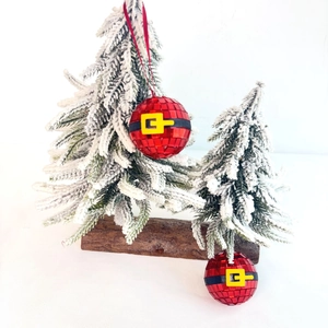Close-up of red disco ball Christmas ornaments with Santa belt detail on a snow-dusted tree