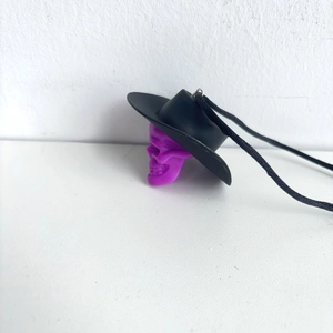 Close-up of a purple skull pendant wearing a black cowboy hat with a black woven cord