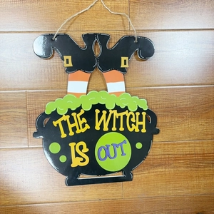 Halloween witch legs in a cauldron hanging sign with The Witch Is Out slogan decor