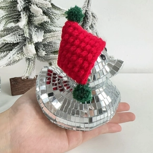 Close-up of a disco mirror duck figurine with a red Christmas knit hat on a palm