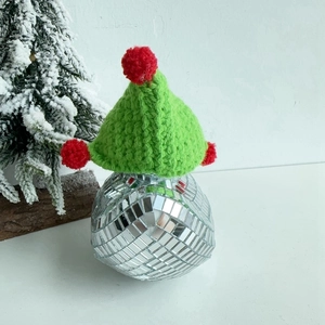 Close-up of green knitted Christmas hat with red pom-poms on a disco ball base