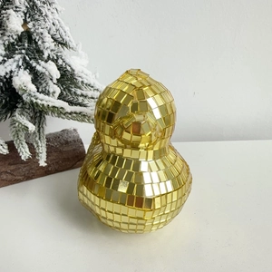 Close-up of golden disco mirror duck figurine beside a miniature snowy Christmas tree