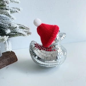Close-up of disco ball duck with red Christmas hat beside a snowy decorative tree
