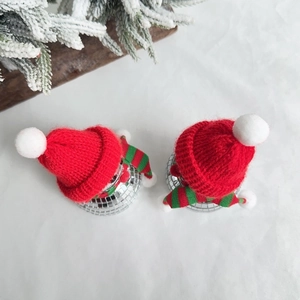 Disco mirror ball ornaments with red hats and striped scarves on white fabric background