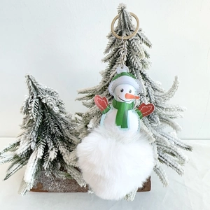 Christmas snowman keychain with white faux fur pompom hanging on a festive tree branch