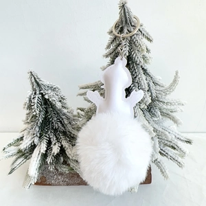 Detail of a white faux fur snowman keychain with silver ring against a snowy tree backdrop