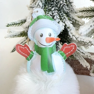 Detailed view of plush snowman keychain with white fur pom-pom on snowy Christmas tree