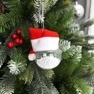 Clear Christmas ornament with white snow filling and Santa hat hanging on a tree branch