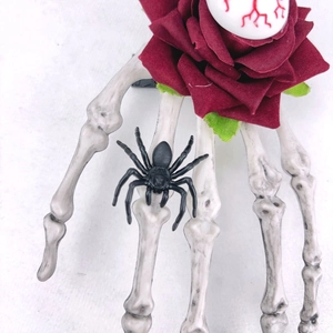 Détail pince à cheveux main de squelette avec rose rouge, œil ensanglanté et araignée