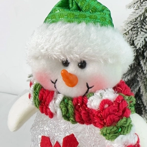 Close-up of a plush snowman decoration with a green sequin hat and knitted scarf