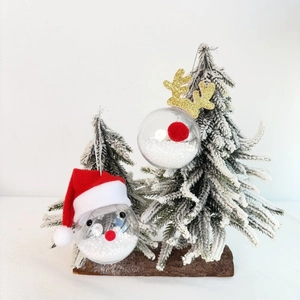 Christmas transparent baubles with reindeer antlers and mini Santa hat on a snow tree